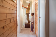 [image] father standing on a stool hanging up a picture up in a house hallway with his son watching